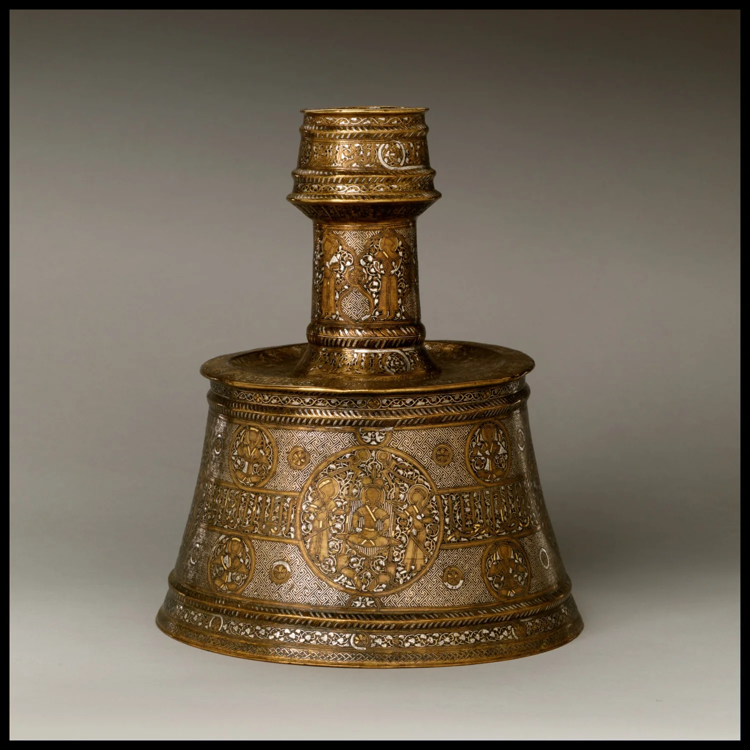 Candelero medieval de latón con incrustaciones de plata y oro, inscripciones y decoración figurativa