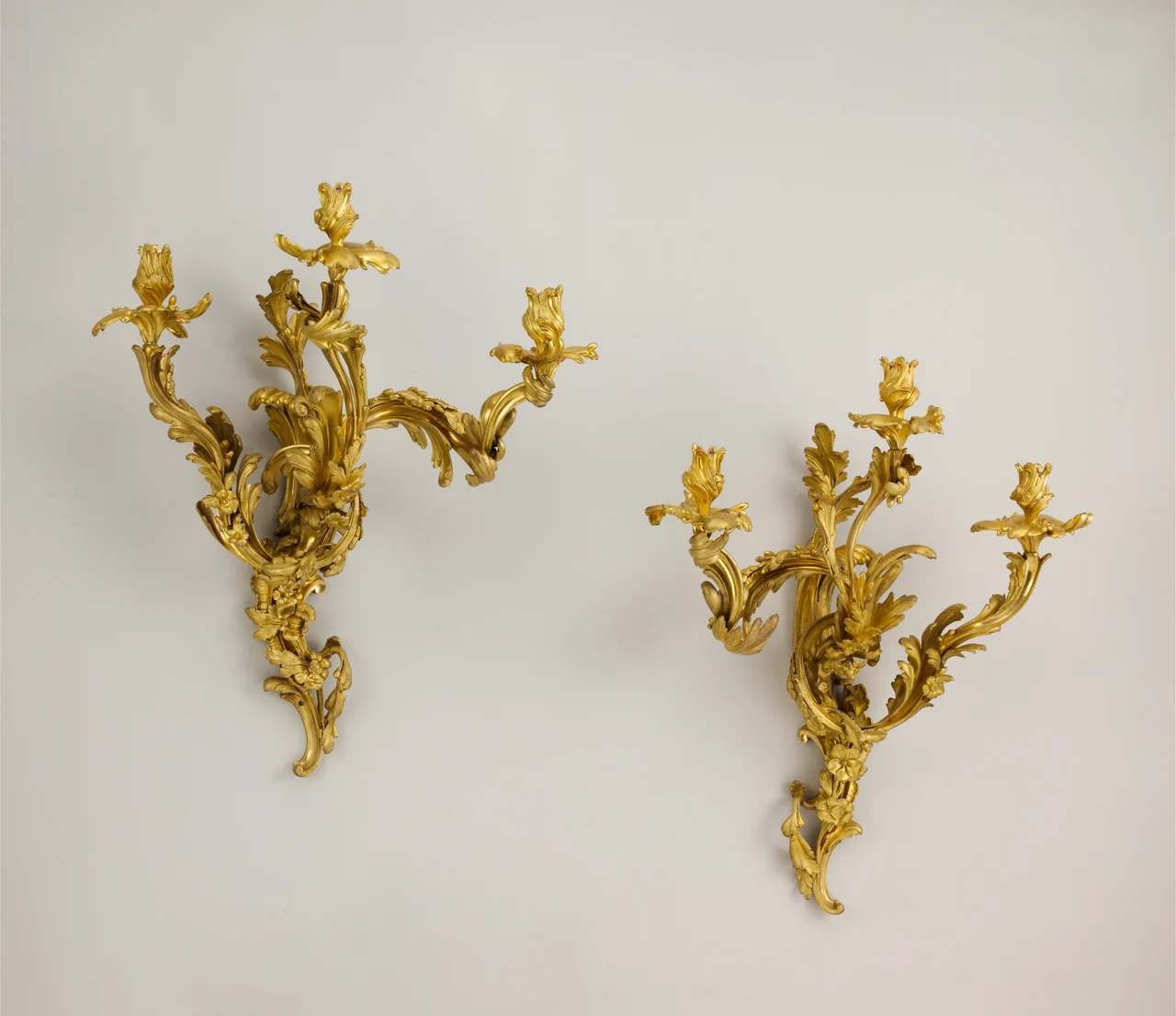 Dos apliques parisinos de tres luces de hacia 1750, en bronce dorado, con ramas curvas, hojas y rocalla